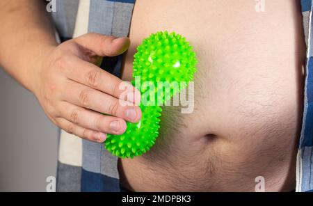 Ein Mann in einem Hemd rollt ein Bauchmassager, um Fett zu verbrennen. Anti-Cellulite-Verfahren. Abnehmen. Übergewicht Stockfoto