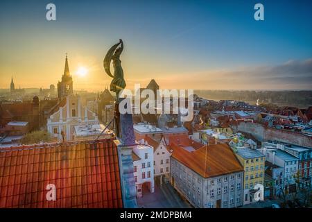Morgendämmerung über den Dächern der Altstadt von Toruń mit einer Skulptur einer Frau im Vordergrund Stockfoto