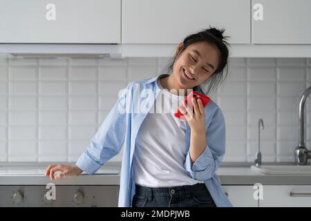 Eine glückliche asiatische Frau wurde mit einem Telefon und einem Lächeln beeindruckt, nachdem sie eine süße Nachricht von ihrem Freund gelesen hatte Stockfoto
