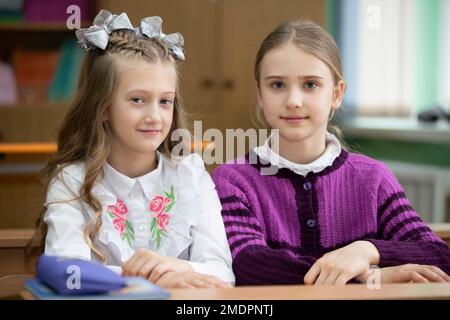 Zwei Schulmädchen sitzen im Klassenzimmer an einem Schreibtisch und schauen in die Kamera. Stockfoto