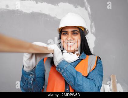 Eine attraktive südasiatische Frau trägt eine Holzplanke in Baukleidung Stockfoto