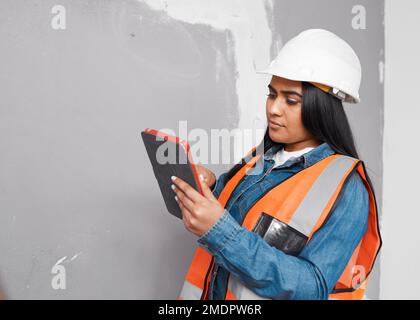 Eine junge, südasiatische Bauarbeiterin verwendet ein Tablet, um ein Projekt zu protokollieren Stockfoto