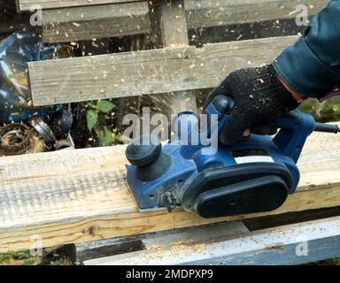 Ein Mann arbeitet mit einem Elektrowerkzeug mit einer elektrischen Hobelmaschine, reinigt altes Holz. Stockfoto