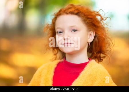 Das Gesicht eines rothaarigen Mädchens, Nahaufnahme vor dem Hintergrund eines Herbstparks. Das Kind im Herbst. Stockfoto