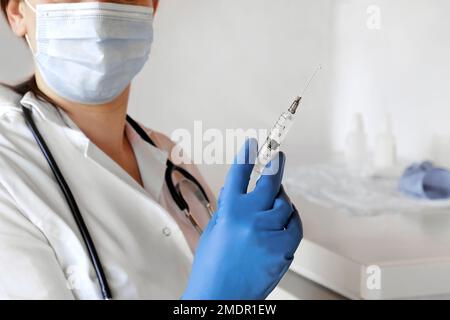 Krankenschwester drückt Luft aus der Spritze für die Impfstoffinjektion. Arzt trägt blaue Handschuhe und medizinische Maske. Eine Person hält eine Spritze mit dem Arzneimittel in der Hand Stockfoto