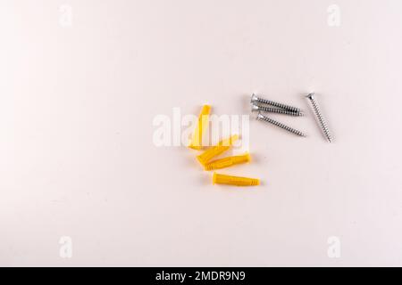 Set aus Schrauben und gelben Kunststoff-Schraubdübel mit isoliertem Textbereich auf weißem Hintergrund bei Aufnahmen mit selektivem Fokus von oben. Stockfoto