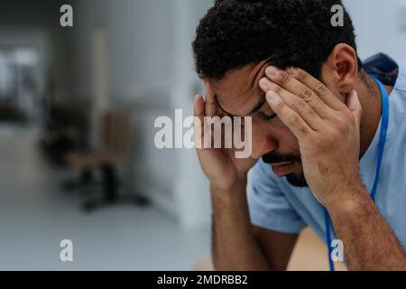 Nahaufnahme eines müden Arztes, der auf dem Krankenhausflur sitzt. Stockfoto