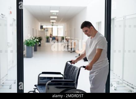 Junger Mann mit Down-Syndome, der im Krankenhaus als Betreuer arbeitet. Das Konzept der Integration von Menschen mit Behinderungen in die Gesellschaft. Stockfoto