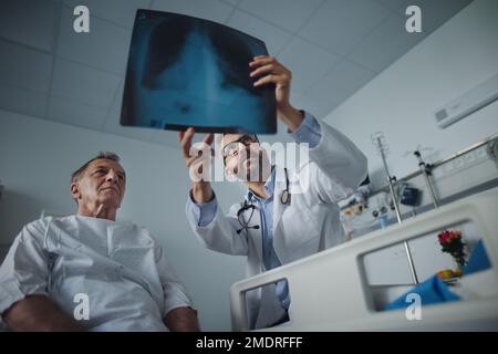 Der reife Arzt zeigt ein Röntgenbild der Lunge des älteren Patienten. Stockfoto