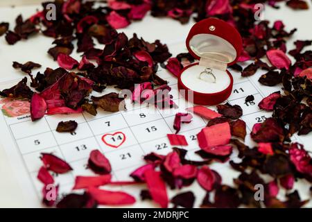 Die Ringbox wird auf den Kalender gesetzt. Der Valentinstag ist im Kalender rot markiert. Heiratsantrag am Valentinstag Stockfoto