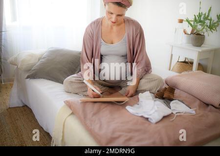 Ein Blick aus einem großen Winkel auf eine schwangere Frau, die ihr Fälligkeitsdatum im Kalender markiert. Stockfoto