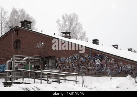 Fotoshooting in einer alten Fabrik, Graffiti-Kunstmauern, alten Industriebauten und eiskaltem Winterwetter. Schnee auf dem Boden Stockfoto