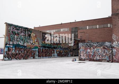 Fotoshooting in einer alten Fabrik, Graffiti-Kunstmauern, alten Industriebauten und eiskaltem Winterwetter. Schnee auf dem Boden Stockfoto