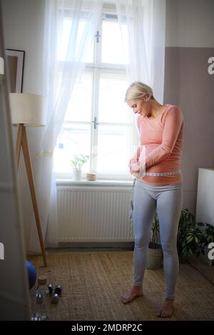 Glückliche Frau, die ihren schwangeren Bauch zu Hause misst. Stockfoto