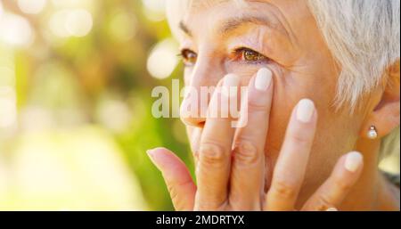 Die traurige Nostalgie der verstorbenen Jugend. Nahaufnahme einer traurigen Seniorin, die sich draußen Tränen aus dem Gesicht wischte. Stockfoto