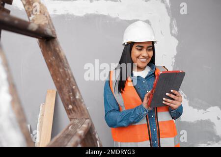 Eine junge, südasiatische Bauarbeiterin verwendet ein Tablet, um ein Projekt zu protokollieren Stockfoto