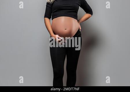 Nahaufnahme einer jungen schwangeren Frau, die ihren Bauch berührt und sich um ihre Gesundheit kümmert. Schwangerschaft, Mutterschaft, Vorbereitung und Erwartungskonzept. Stockfoto