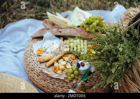 Wein und verschiedene Produkte für das Sommerpicknick werden auf einer Decke im Freien serviert Stockfoto