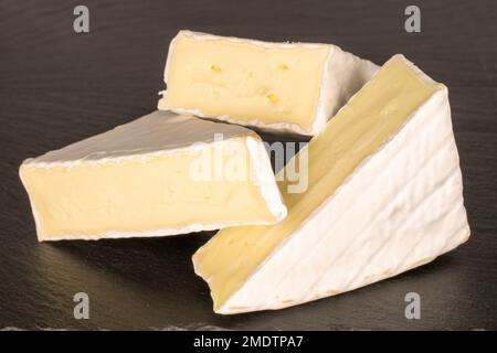 Drei Stücke duftenden Brie-Käse auf Schieferstein, Makro. Stockfoto