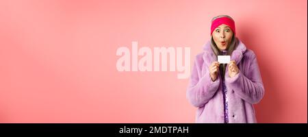 Shopping- und Modekonzept. Bild von erstaunt asiatische ältere Frau Auschecken Promo-Angebot, halten Kunststoff-Kreditkarte und starren beeindruckt in die Kamera Stockfoto