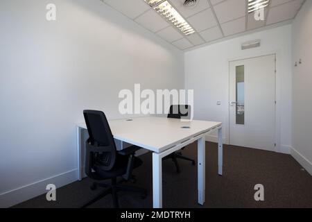 Büro mit doppelten weißen Holztischen mit weißen Methacrylat-Trennwänden und schwarzen Drehhockern und einer Tür mit länglichem Glas Stockfoto