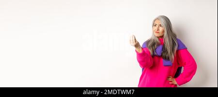 Mürrische asiatische Großmutter beschwert, zeigt italienisch, was Sie wollen Geste, schüttelt die Finger und starrte wütend links auf den Kopierraum, über stehen Stockfoto