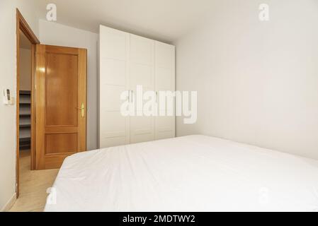 Schlafzimmer mit einem Doppelbett, einem weißen dreiteiligen Kleiderschrank und einer Eichentür Stockfoto