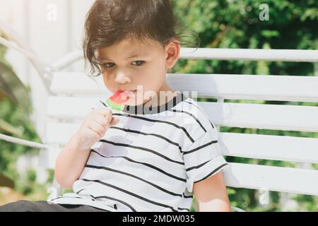 Süßes lateinindisches Kind, das süßes Fruchteis isst, draußen im Freien, farbenfroh schön. Stockfoto