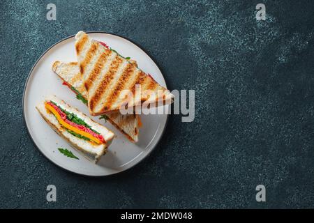 Drei hausgemachte Sandwiches mit Wurst, Käse und Rucola auf dunklem Betonhintergrund Stockfoto