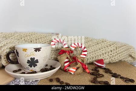 Eine Weihnachtstischszene mit einer Tasse Kaffee, zwei dekorativen Zuckerstangen und einem Weihnachtsbaum aus Kaffeebohnen mit einem kleinen Weihnachtsmannmütze auf der Oberseite. Stockfoto