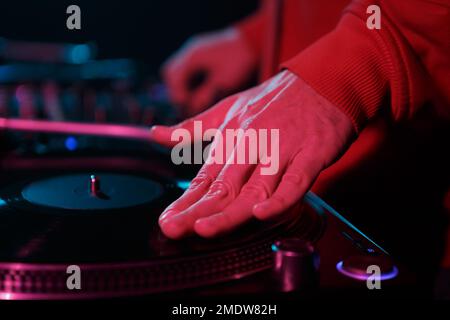 Hip-Hop-DJ kratzt Vinylscheiben in roten Bühnenlichtern auf dem Plattenspieler. Hand des Disc-Jockey kratzt die Disc in Nahaufnahme Stockfoto