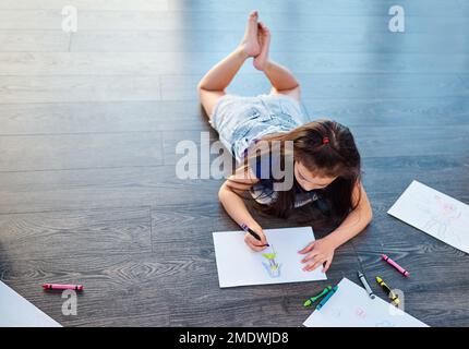 Sie lebt ein Leben voller Farben. Bild eines jungen Mädchens, das auf dem Boden liegt und in Bildern in ihrem Malbuch zu Hause ausmalt. Stockfoto