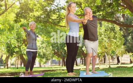 Sein sportlicher Geist ist für immer jung. Ein junger Lehrer, der ein Seniorenpaar in einem Yoga-Kurs leitet. Stockfoto