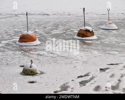 See mit roten Ankerbojen, die im Winter im Eis gefroren sind. Stockfoto