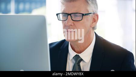 Seine E-Mails für heute durchgehen. Ein reifer Geschäftsmann, der an einem Computer in einem Büro arbeitet. Stockfoto