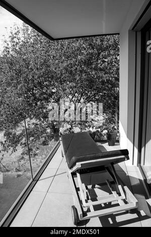 Liegestuhl auf einem modernen Balkon mit Kirschbaum an einem sonnigen Sommertag in der schweiz. Stockfoto