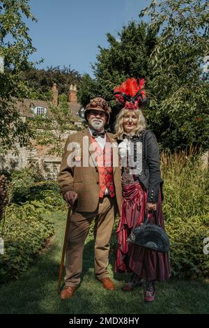 Ein exzentrisches Paar mittleren Alters, das im Garten eines Landhauses steht. Gut gekleidetes Steampunk-Paar mittleren Alters. Lotteriegewinn, Reisekonzept. Stockfoto