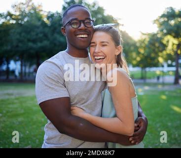 Liebe, Rassenfreunde oder ein paar Freunde umarmen sich bei einem romantischen Date in einem Park und verbinden sich in der Natur miteinander. Romantik, lustiger schwarzer Mann und lachende Frau Stockfoto