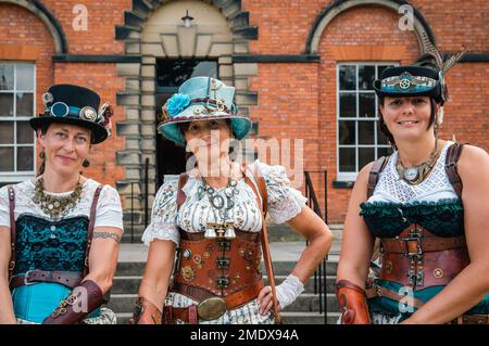 Drei weibliche Steampunks lächeln, wenn sie direkt in die Kamera schauen. Stockfoto