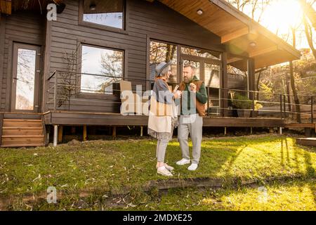 Glücklicher Mann und glückliche Frau stehen neben ihrem neuen Haus und lächeln Stockfoto