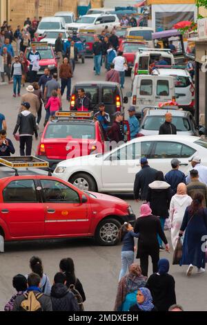 Fez, Marokko - Verkehr von Fußgängern, Autos, roten Petit Taxis auf der Straße vor der autofreien Medina Fes el Bali. Belebter Absetzpunkt. Pulsierende Stadtlandschaft. Stockfoto