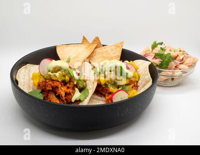 Gesunde vegane Jackfrucht-Tacos in einer schwarzen Schüssel auf weißem Hintergrund. Stockfoto