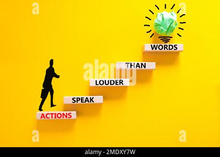 Das Symbol „Aktionen sprechen lautere Wörter“. Begriffe Taten sprechen lauter als Worte auf Holzblöcken. Wunderschöner gelber Hintergrund für den Tisch. Geschäftlich Stockfoto
