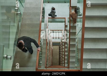 Über dem Bild von drei Geschäftsleuten in formeller Kleidung, die auf dem Weg zur Arbeit nach oben und zwischen den Treppen in einem modernen Gebäude gingen Stockfoto