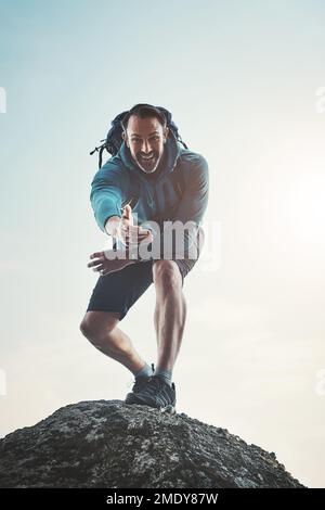 Nimm meine Hand und lass uns die Welt gemeinsam erobern. Niedrig angewinkeltes Porträt eines Mannes mittleren Alters, der auf einem Felsen steht und seine Hand ausstreckt. Stockfoto