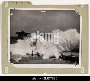 Wellenbrecher gesunkener Schiffe Shielded Landings in der Normandie bei Gewaltsturm. Der strategische Untergang von 23 Frachtern, Bug bis Heck, am D-Day Plus One and Two, schuf einen Wellenbrecher, hinter dem die alliierten Invasionsschiffe während eines wütenden Sturms, der die Strände der Normandie zerrissen hat, Truppen und Vorräte entluden. Sechs Küstenwachbeamte, alle Experten im Umgang mit heimtückischen Surfströmungen, nahmen an der Überwachung der Sinkings Teil und wurden für ihre effiziente Erfüllung der Aufgabe gelobt. Hier schlägt eine bergige Welle gegen eines der gesunkenen Schiffe, während die Landung voranschreitet. Stockfoto