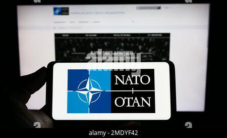 Person, die ein Smartphone mit dem Logo der Nordatlantischen Vertragsorganisation (NATO) auf dem Bildschirm vor der Website hält. Konzentrieren Sie sich auf das Display des Telefons. Stockfoto