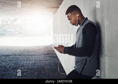 Ich bin fast fertig... ein gutaussehender junger Mann, der eine SMS schickt, während er draußen trainiert. Stockfoto
