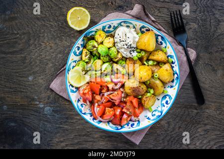 Rosenkohl und Tomatensalatschüssel, gesunde und ausgewogene Speisen mit gebackenen Kartoffeln Stockfoto