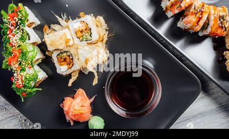 Ein paar Sushi-Brötchen auf schwarzen Steintellern, serviert mit Sojasauce und Wasabi Stockfoto